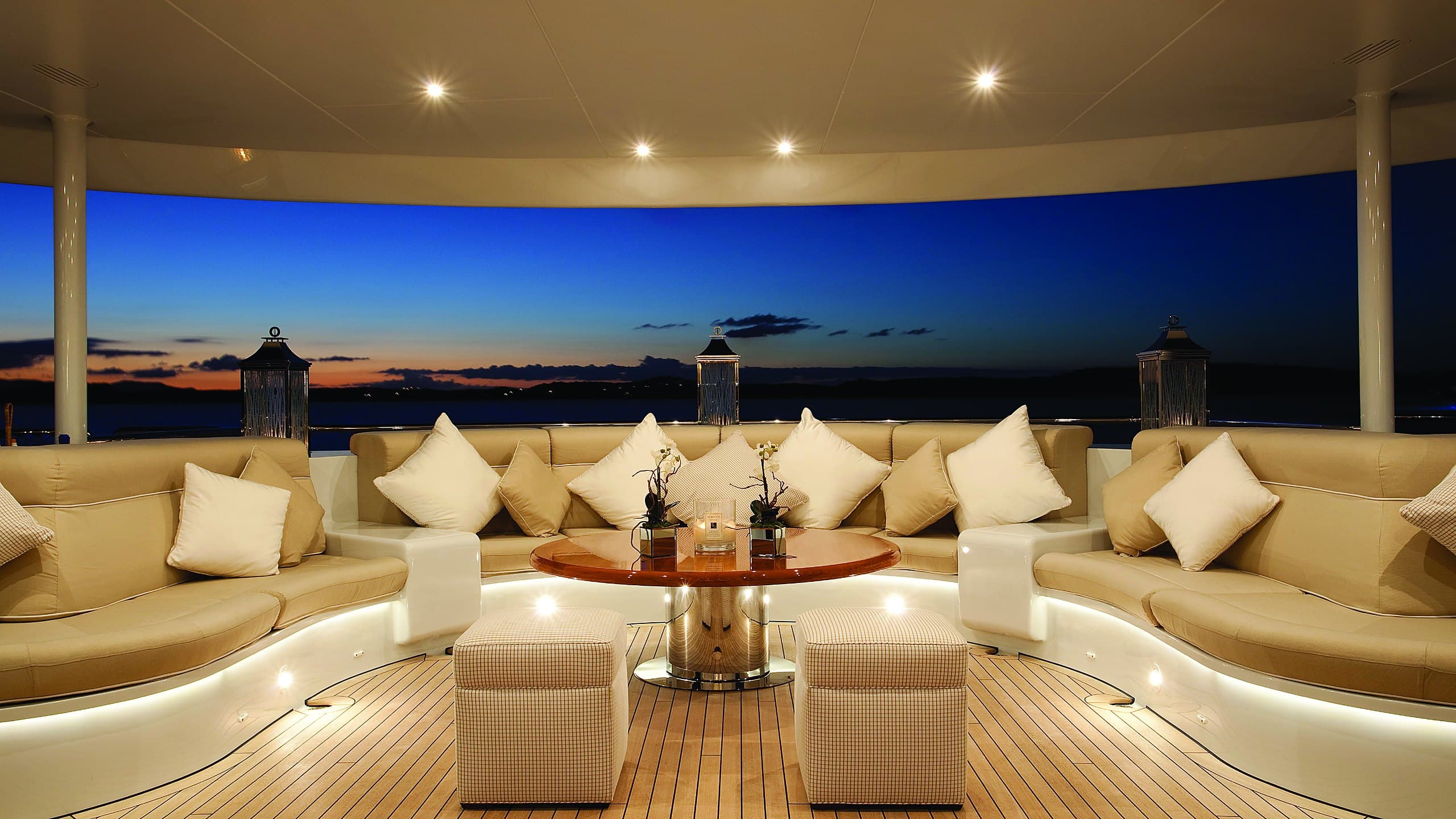 Superyacht aft-deck lounge at dusk with layered Lutron lighting — warm cove and deck lighting beneath a twilight sky